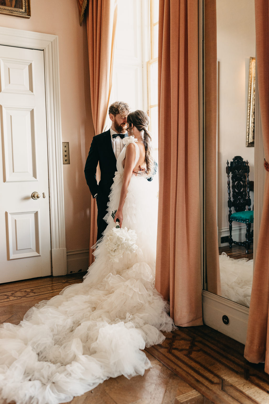 Bride in a white ruffled Millia London wedding dress with the groom in black tie  in the music room of Stansted House, Stansted Park