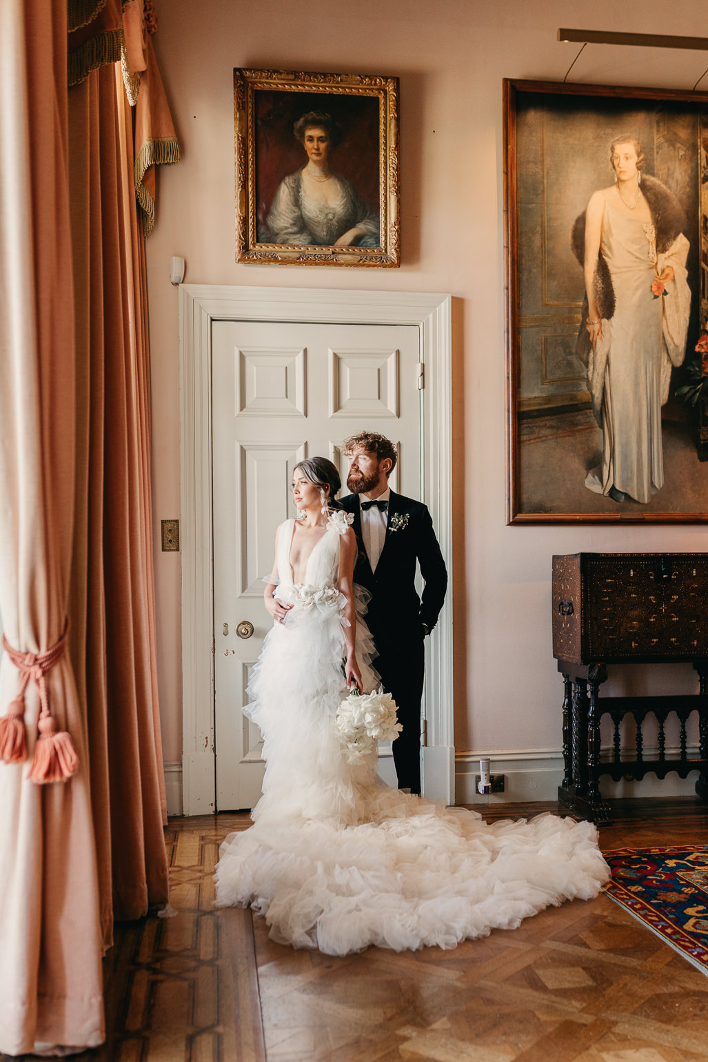 Bride in white ruffled Millia London wedding dress with groom in black tie  in the music room of Stansted House